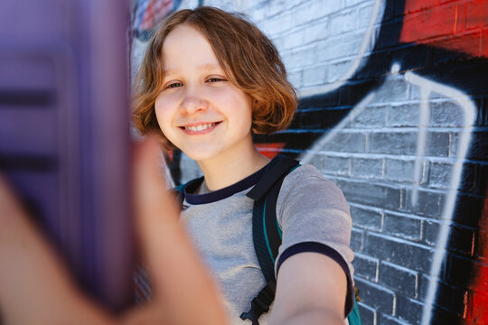 A smiling girl takes a selfie with a smartphone outdoors by a wall
