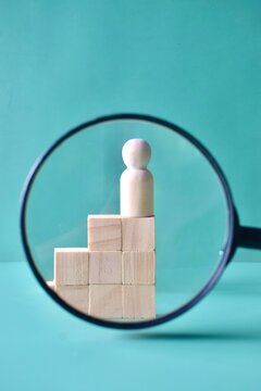 A business audit and talent hunting concept featuring a wooden figure on a block staircase framed by a magnifying glass.