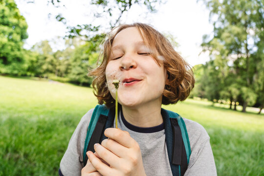 Happy girl blows a dandelion outdoors in a green park