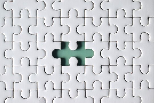 A direct macro top view centered on a single missing piece hole within a white jigsaw puzzle grid, exposing the solid light green surface underneath.