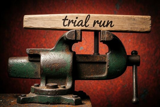 Old vise tool grips wooden plank with text trial run. Represents pressure stress challenge. Concept of testing limits or difficult situations met with force.
