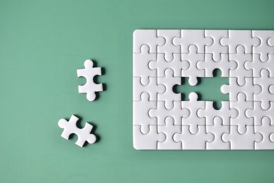 Top-down view of an unfinished white jigsaw puzzle on a mint green background with a large gap and two separate matching pieces laying to the left.