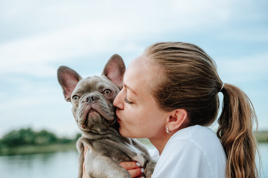 A woman kisses her french bulldog near a river