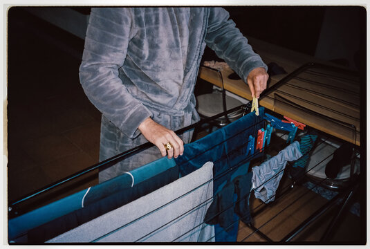 Man in bathrobe hanging laundry on drying rack indoors at night