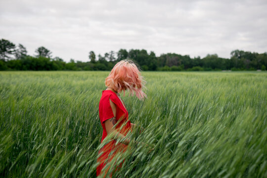 Woman in a red dress stands in a green wheat field