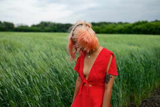 Woman in a red dress stands in a green wheat field during summer