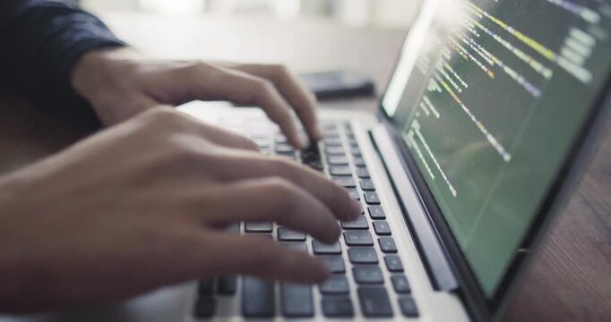 Programmer types on a laptop while working with multiple lines of software code visible on the display.