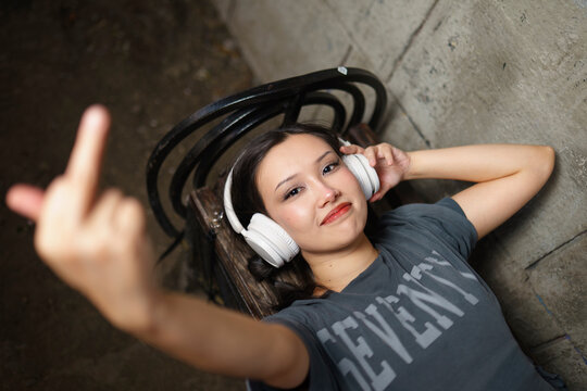 Young woman on a bench listens to music and shows her middle finger