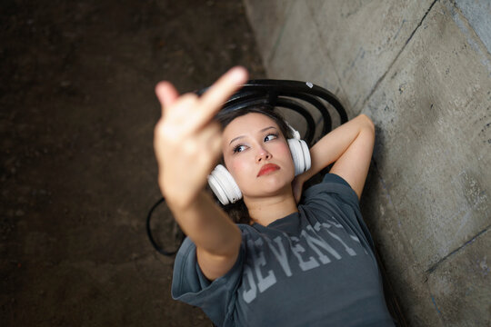 Young woman on a bench shows middle finger while listening to music