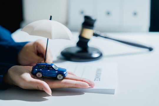 Car insurance policy protection concept with judge gavel on document, person feeling secure and safe protecting vehicle toy with umbrella