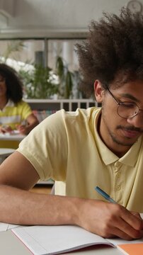 Concentrated victim African American student guy writing notes study in class bullying by classmates laugh throwing crumpled papers balls racism discrimination man male feeling bad bullied by students