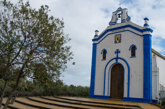 Blue and white church Ermita de Nuestra Se&ntilde;ora del Carmen, a tree in foreground, white clouds, Ayamonte, Spain 
