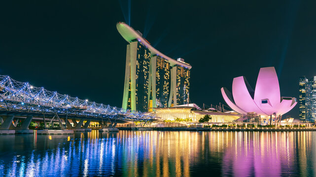 Marina Bay waterfront skyline in Singapore at night, Marina Bay Sands, ArtScience Museum, and Helix Bridge illuminated against dark sky, colorful reflections, calm water