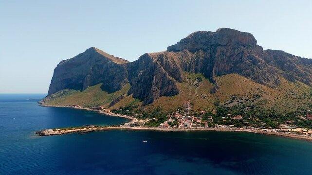 Daytime aerial perspective of the Capo Gallo nature reserve in Palermo, Sicily. The rugged mountains meet the pristine Mediterranean coastline under clear skies.