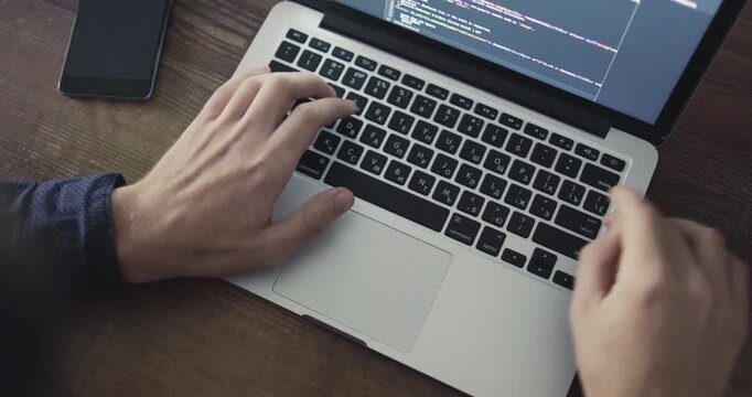 Close-up of software development on a laptop with colorful source code visible on screen and a phone on the table.