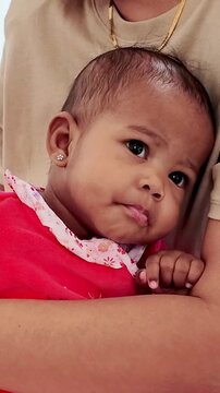 Close-up of a baby in a red outfit resting in an adult"s arms, gazing softly to the side, conveying warmth, safety, and affection.