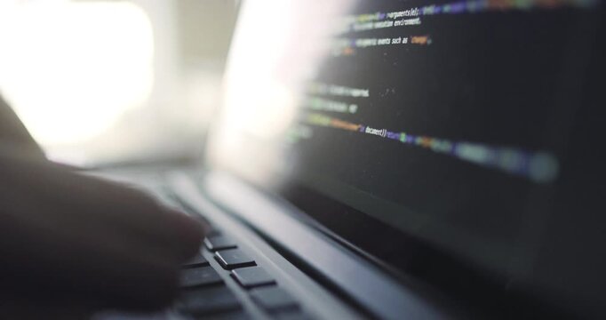 Shallow focus view of a laptop display showing software code as hands work on the keyboard.
