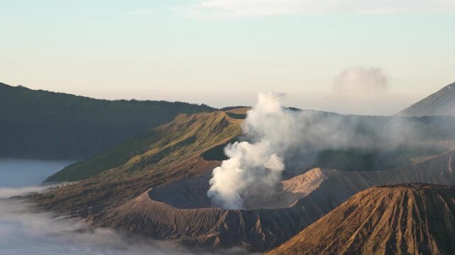 Volcanic smoke rises from Mount Bromo crater at sunrise in a misty mountain landscape