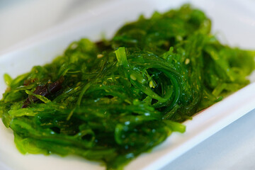 Close up shot of vibrant green chuka wakame seaweed salad served on a white rectangular plate. Healthy Asian appetizer with seasoned sesame seeds and translucent texture. © Ekaterina