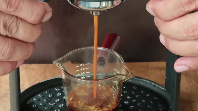 Close up of a manual lever espresso machine brewing a fresh shot of coffee with thick into a clear plastic measuring cup.