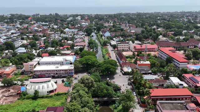 Fly high over the iconic water channels of Kerala. A sweeping drone perspective showing Alappuzha's Commercial Canal and CCS SB Road in Civil Station Ward stretching through dense green trees