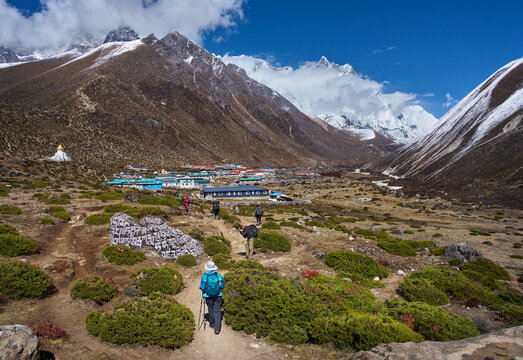 Group Hikers walking on the trail towards Dingboche village with colorful houses and snow-capped Himalayan peaks on Everest Base Camp route.