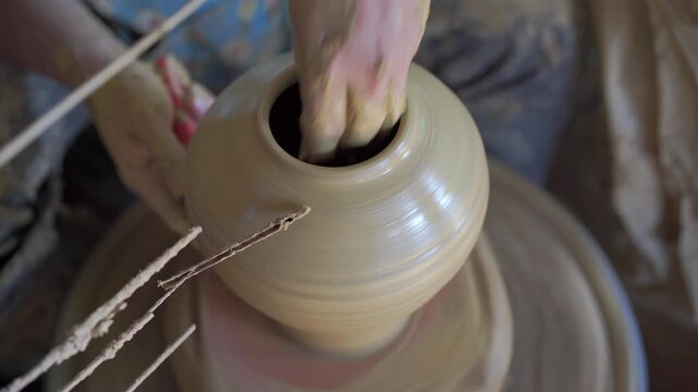 Male hands make wet clay on a potter's wheel, sculpting a vessel in a fast-moving circle in a clay pot, shaping raw clay, and practicing traditional craft. Ancient handmade craft work.  