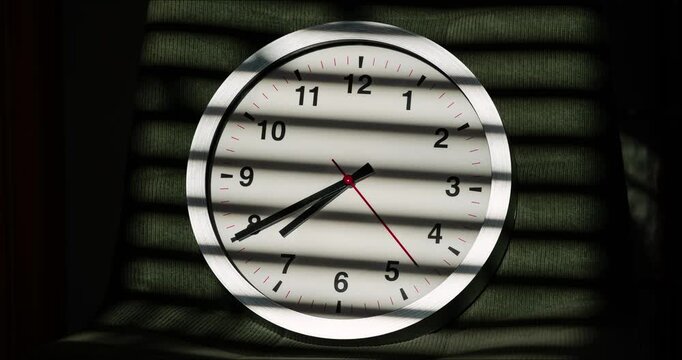 Timelapse of analog wall clock with moving hands and window blind light shadow