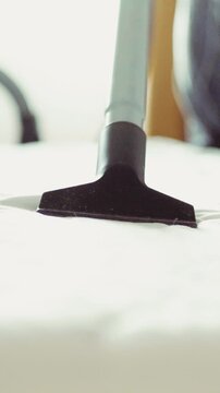 Cleaning dust and crumbs off a white mattress surface with a vacuum
