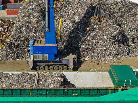 Blue Crane Loading Scrap Metal Into a Cargo Ship at an Industrial Port During Daylight