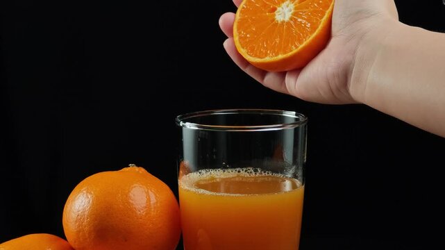 Squeeze juice from orange. Woman hand squeezes half orange into aclear glass.