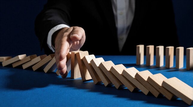 Hand stops falling dominoes. Businessman prevents chain reaction, shows business risk control and crisis management strategy. Planning and intervention stop cascade.