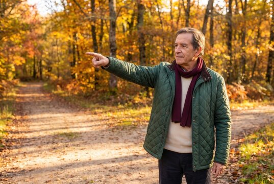 Senior man pointing forward on a path, exploring autumn nature