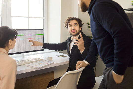 Team meeting discussion with colleagues analyzing data. Manager leads a presentation on a large monitor, pointing at key trends. Bright office setting. Concept of teamwork and leadership.