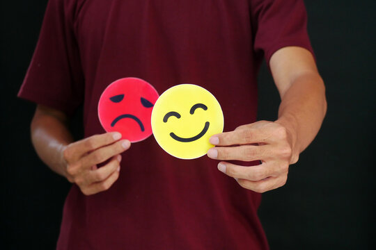 Person holding red sad and yellow happy icons illustrating emotional swings, mental health assessment, and mood tracking against black background.