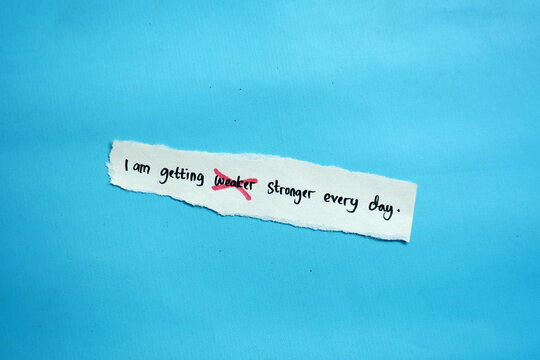 Hand-torn paper showing "I am getting weaker stronger every day" with "weaker" crossed out for mental health resilience.