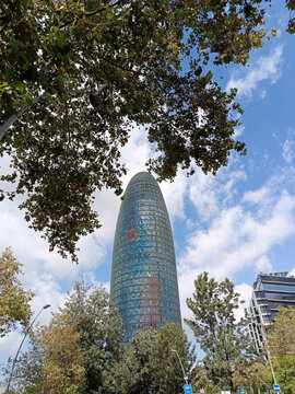 Barcelona, Spain - October 1, 2025: Torre Glories skyscraper surrounded by trees under blue sky