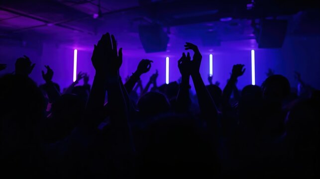 Crowd of people with hands raised dancing in nightclub under purple neon light. Silhouette of woman and man enjoying electronic music at dance festival. Nightlife party entertainment.