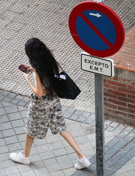 Mujer con tel&eacute;fono m&oacute;vil adicta al smartphone celular por la calle adicci&oacute;n y nomofobia con pantal&oacute;n corto y zapatillas paso por se&ntilde;al de tr&aacute;fico