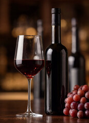 Fototapeta premium A bottle of red wine with a filled glass and a cluster of grapes on a warm blurred background. The composition evokes tasting, dining, and cozy evening ambiance.