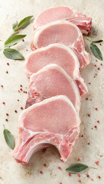 Raw pork loin chops arranged in a row on a light surface with fresh sage leaves and scattered pink peppercorns. Clean composition suitable for food or recipe use.