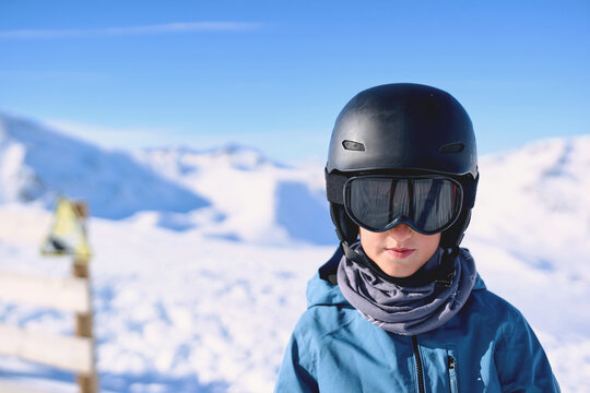 Boy wearing ski helmet and goggles in snowy mountains, close up portrait.