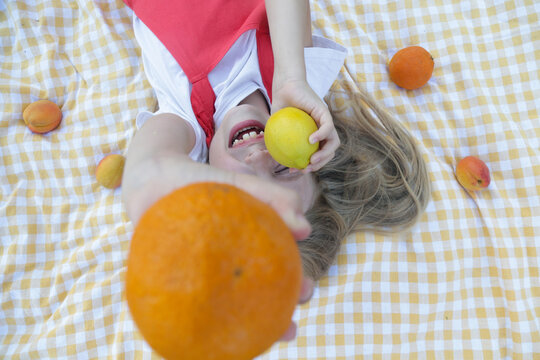 Top view of a happy little girl having fun with fresh citrus fruits on a picnic blanket