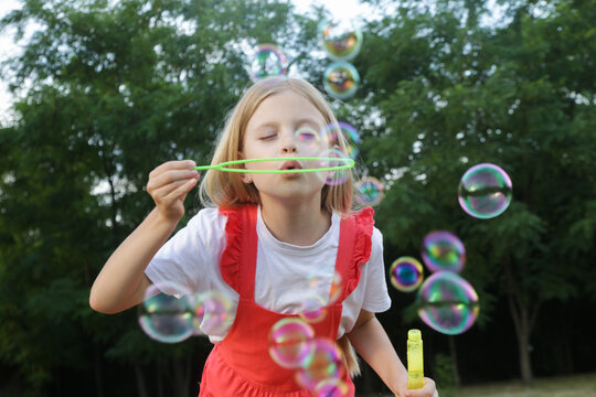 Happy little girl blowing soap bubbles on a sunny summer day