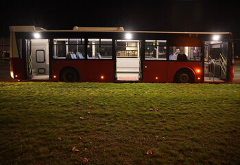 almost empty modern red city bus with open door on urban road at night dusk. Side view Green grass floor flooring © Maxim Chuev