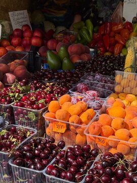 Fresh seasonal fruits, berries, vegetables and herbs displayed at a local farmers market stall. Colorful assortment of natural produce including apricots, plums, cherries and greens.