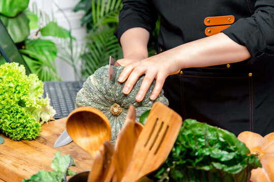 Hands of woman cutting raw green pumpkin with knife on wooden board. Healthy vegetarian cooking and autumn recipe concept