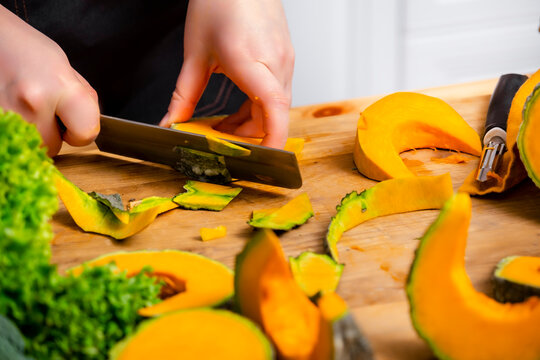 Woman hands slice raw pumpkin with cleaver on cutting board. Domestic culinary food preparation concept.