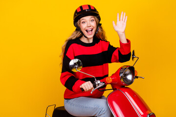 Obraz premium Cheerful young woman riding a retro scooter in trendy outfit on yellow background showcasing fun and stylish lifestyle
