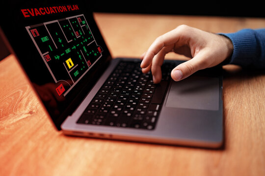 Hands using a laptop to review an emergency evacuation plan on a computer screen indoors
